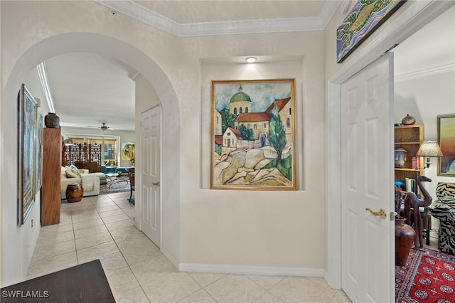 hall featuring ornamental molding, arched walkways, baseboards, and light tile patterned floors