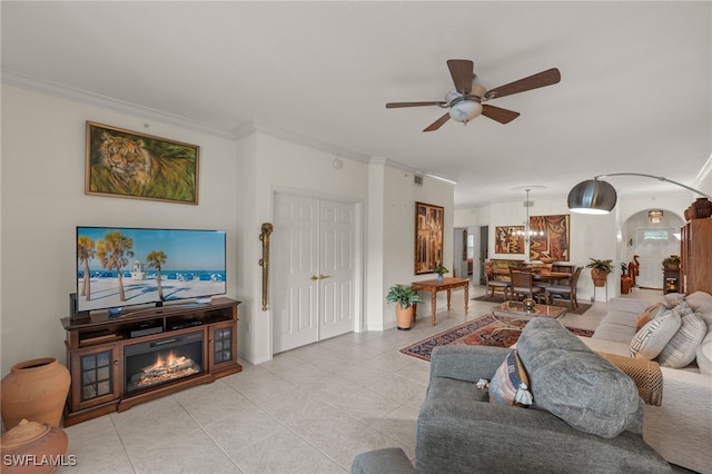 living room with arched walkways, light tile patterned floors, ceiling fan with notable chandelier, a glass covered fireplace, and crown molding