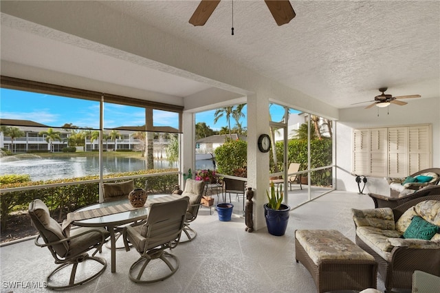 sunroom / solarium featuring a healthy amount of sunlight, a water view, and a ceiling fan