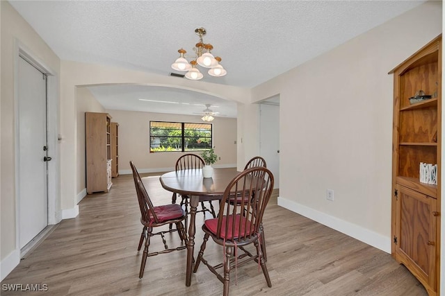 dining room with ceiling fan with notable chandelier, light wood-type flooring, and a textured ceiling