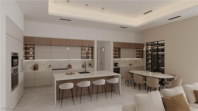 kitchen featuring sink, a raised ceiling, white cabinetry, and an island with sink