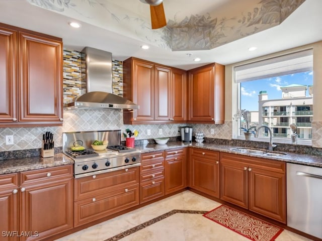 kitchen with appliances with stainless steel finishes, tasteful backsplash, dark stone counters, wall chimney exhaust hood, and sink