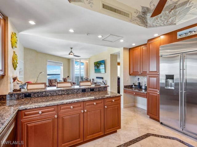 kitchen with dark stone countertops, ceiling fan, and stainless steel built in fridge