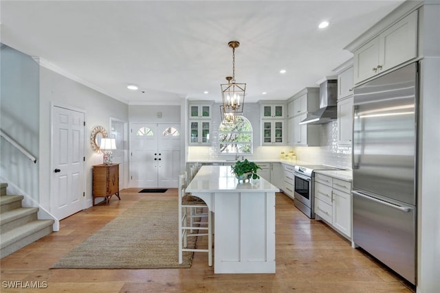 kitchen with wall chimney exhaust hood, tasteful backsplash, decorative light fixtures, a kitchen island, and appliances with stainless steel finishes