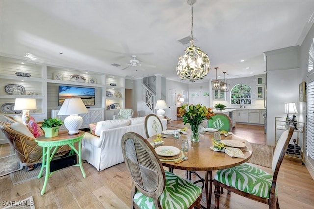 dining space featuring ceiling fan with notable chandelier, light hardwood / wood-style floors, and sink