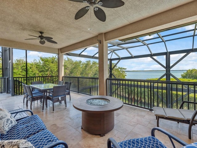 view of patio / terrace with a lanai, ceiling fan, a water view, and a fire pit