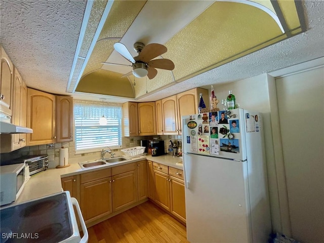 kitchen with white appliances, a raised ceiling, a sink, light wood-type flooring, and backsplash