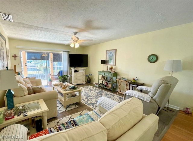 living area with ceiling fan, a textured ceiling, wood finished floors, and visible vents