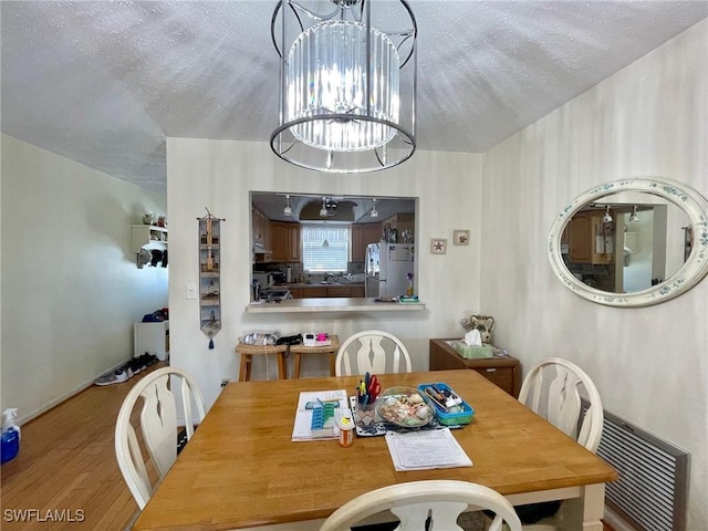 dining space featuring visible vents, a notable chandelier, a textured ceiling, and wood finished floors