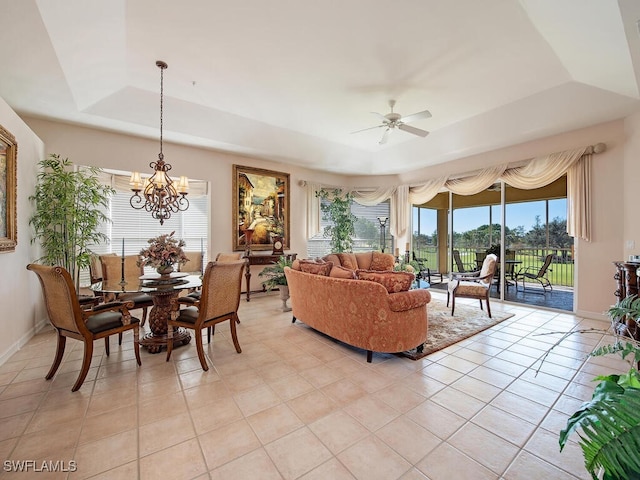 living room with ceiling fan with notable chandelier, light tile patterned floors, and a tray ceiling