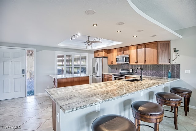 kitchen with sink, appliances with stainless steel finishes, a tray ceiling, light stone counters, and kitchen peninsula