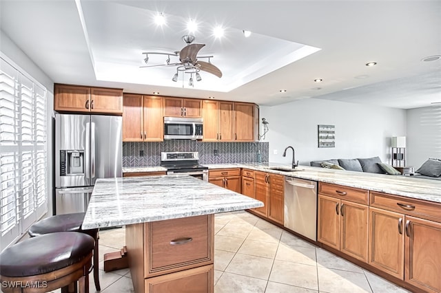 kitchen with a raised ceiling, a breakfast bar, sink, and appliances with stainless steel finishes