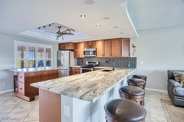 kitchen featuring kitchen peninsula, light stone countertops, stainless steel appliances, a tray ceiling, and sink