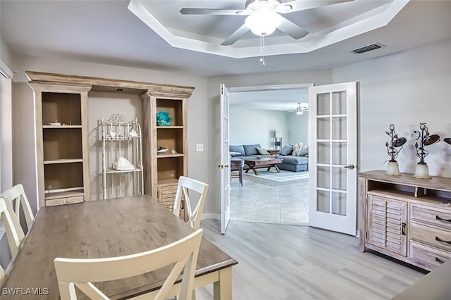 dining area featuring a raised ceiling, ceiling fan, french doors, and light wood-type flooring