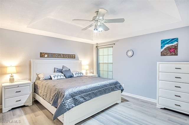 bedroom featuring light wood-type flooring, a tray ceiling, and ceiling fan