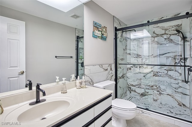 bathroom featuring vanity, a shower with door, tile patterned flooring, toilet, and tile walls