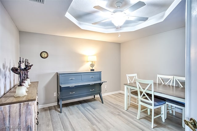 home office featuring a raised ceiling, ceiling fan, and light hardwood / wood-style floors