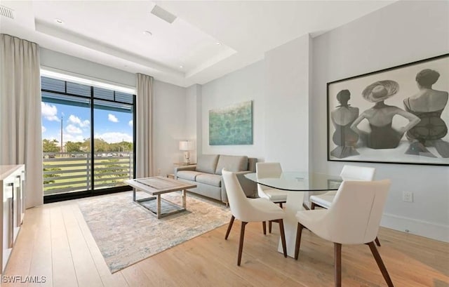 dining area with light hardwood / wood-style floors and a raised ceiling