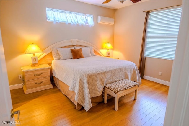 bedroom featuring multiple windows, ceiling fan, a wall mounted air conditioner, and light wood-type flooring