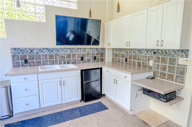 kitchen featuring white cabinets, backsplash, black refrigerator, and sink