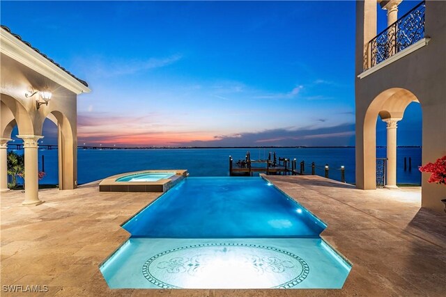 pool at dusk featuring a patio area, an in ground hot tub, and a water view