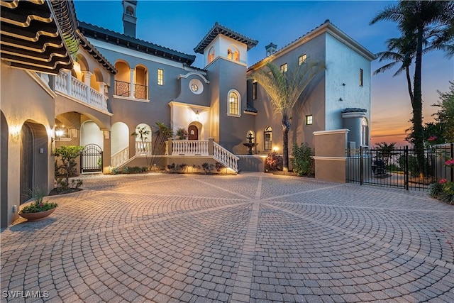 view of front of home with a gate, curved driveway, fence, and stucco siding