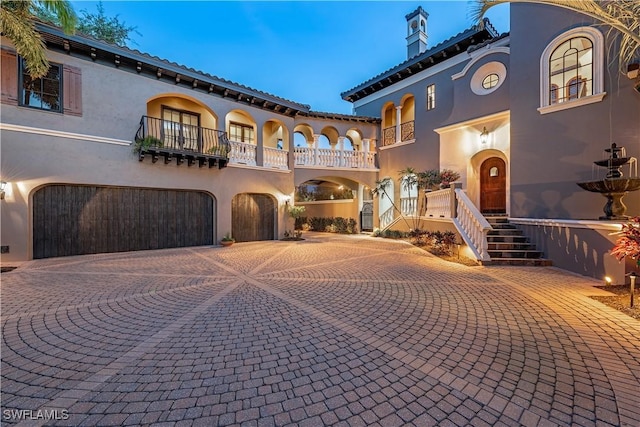 mediterranean / spanish-style house with an attached garage, a chimney, decorative driveway, and stucco siding