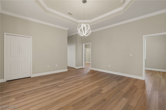 spare room featuring an inviting chandelier, crown molding, a tray ceiling, and light hardwood / wood-style flooring