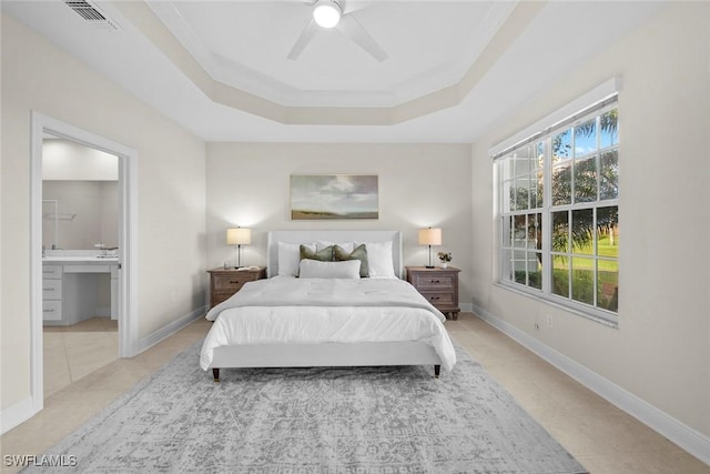 bedroom featuring ensuite bathroom, ornamental molding, a tray ceiling, ceiling fan, and light tile patterned floors