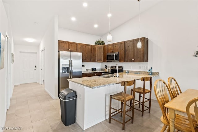 kitchen with kitchen peninsula, light stone counters, stainless steel appliances, decorative light fixtures, and a breakfast bar area