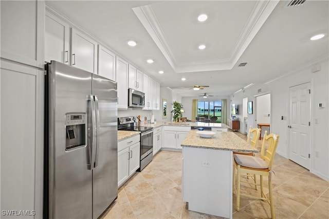 kitchen with white cabinetry, stainless steel appliances, a raised ceiling, kitchen peninsula, and a kitchen bar