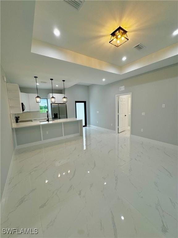 kitchen with stainless steel refrigerator with ice dispenser, a raised ceiling, sink, decorative light fixtures, and white cabinets