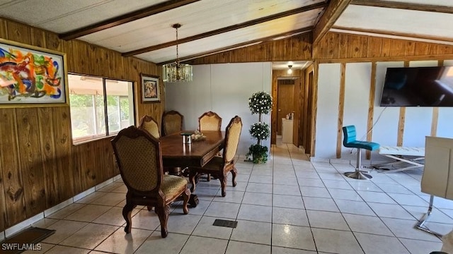 dining area with a notable chandelier, lofted ceiling with beams, wood walls, and light tile patterned floors