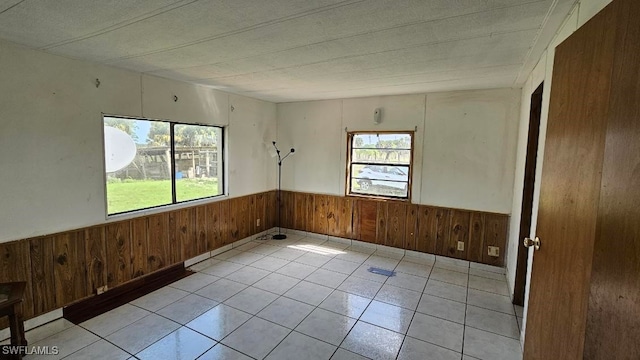 empty room with light tile patterned floors, a textured ceiling, and wooden walls