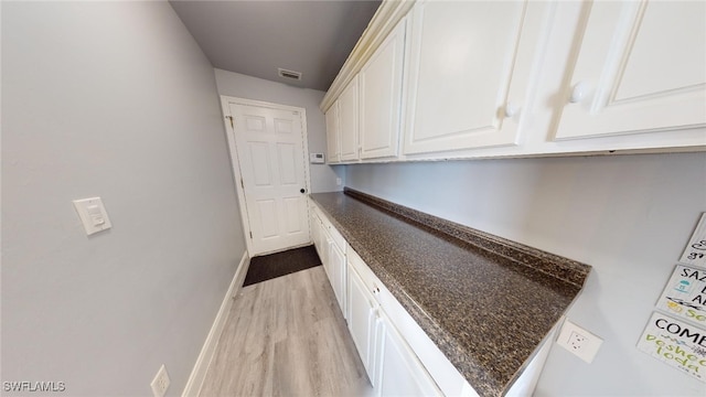 bar with dark stone countertops, white cabinetry, and light hardwood / wood-style flooring