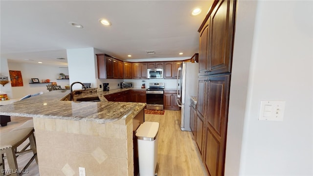 kitchen with stone counters, kitchen peninsula, a kitchen bar, sink, and appliances with stainless steel finishes