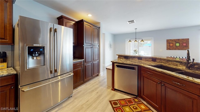 kitchen featuring light hardwood / wood-style floors, sink, hanging light fixtures, appliances with stainless steel finishes, and light stone counters