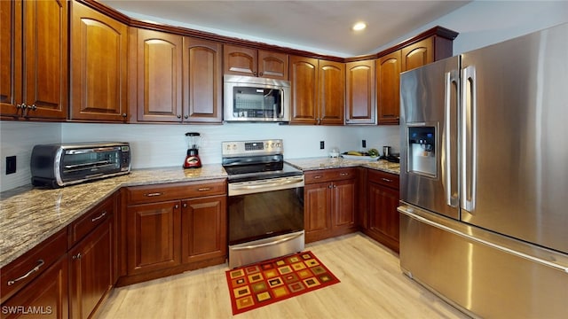 kitchen featuring stainless steel appliances, light hardwood / wood-style flooring, and light stone counters