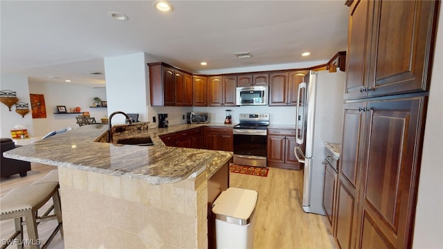 kitchen with kitchen peninsula, a kitchen bar, sink, light stone countertops, and appliances with stainless steel finishes