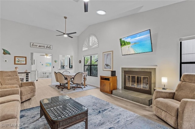 living room featuring light hardwood / wood-style floors, high vaulted ceiling, and a tiled fireplace