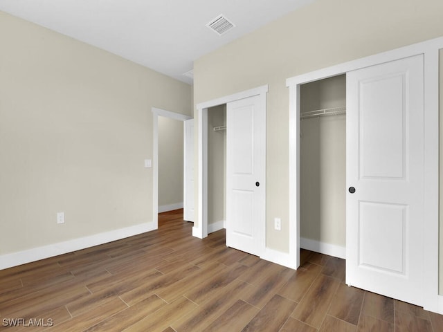 unfurnished bedroom with dark wood-style floors, visible vents, baseboards, and multiple closets