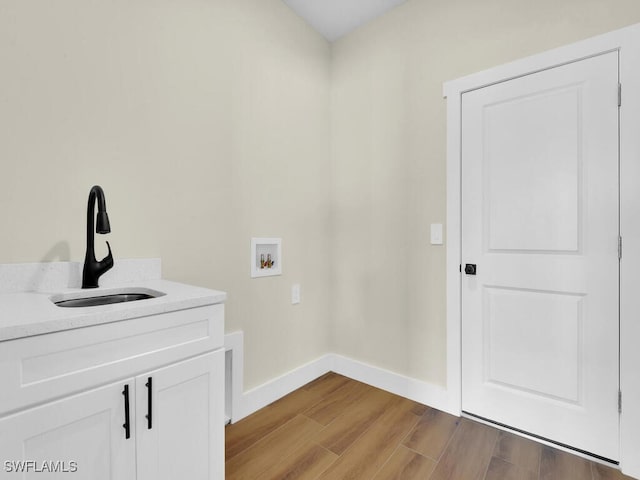 laundry room with cabinet space, light wood finished floors, baseboards, hookup for a washing machine, and a sink