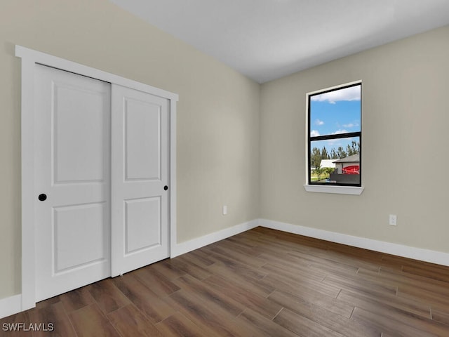 unfurnished bedroom with dark wood-type flooring, a closet, and baseboards