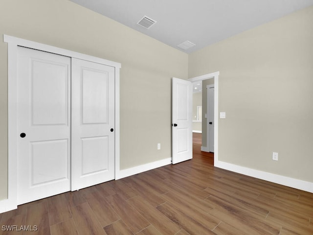 unfurnished bedroom with a closet, dark wood-style flooring, visible vents, and baseboards