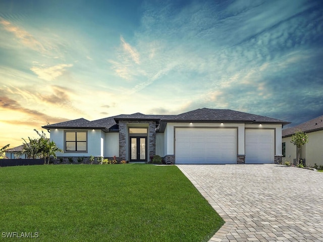 prairie-style home featuring a garage, a lawn, decorative driveway, french doors, and stucco siding