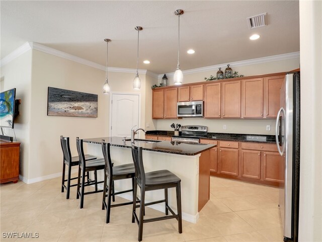 kitchen with appliances with stainless steel finishes, crown molding, sink, decorative light fixtures, and an island with sink