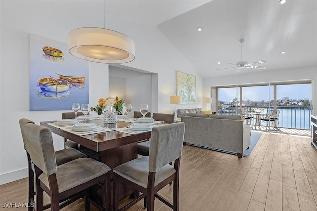 dining area featuring ceiling fan, light hardwood / wood-style floors, high vaulted ceiling, and a water view