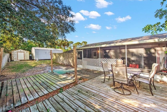 deck featuring an outbuilding, outdoor dining area, a storage unit, a sunroom, and fence