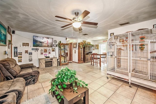 living room featuring light tile patterned floors, ceiling fan, visible vents, and a textured ceiling