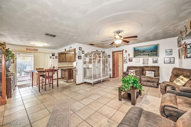 living area with light tile patterned floors, ceiling fan, visible vents, and a textured ceiling